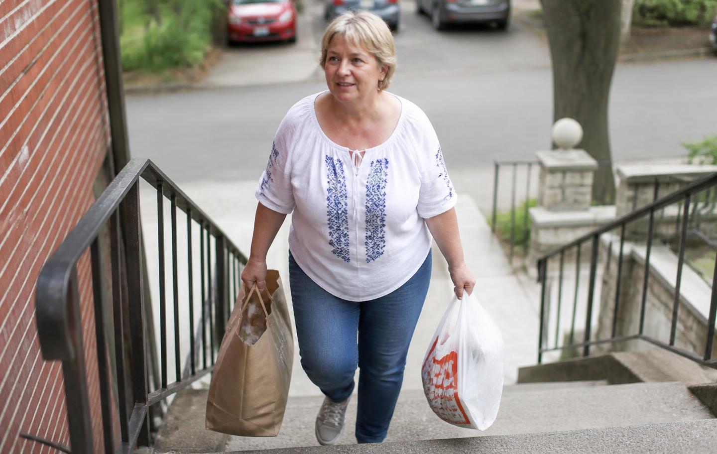 A woman in her late fifties carrying shopping bags confidently up a flight of outdoor steps