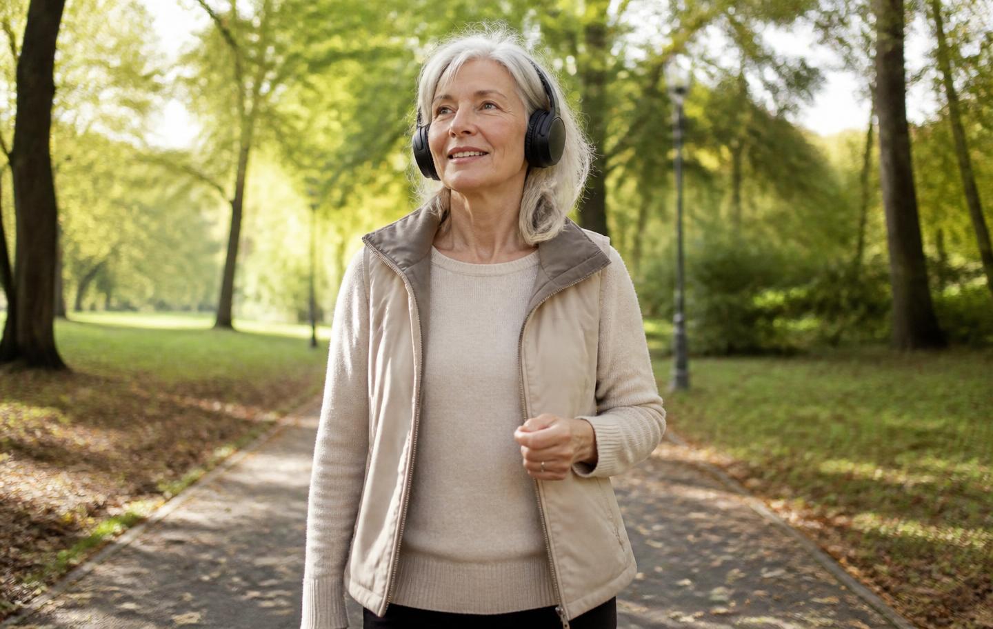 A woman in her sixties listening to a podcast through headphones while walking in a park